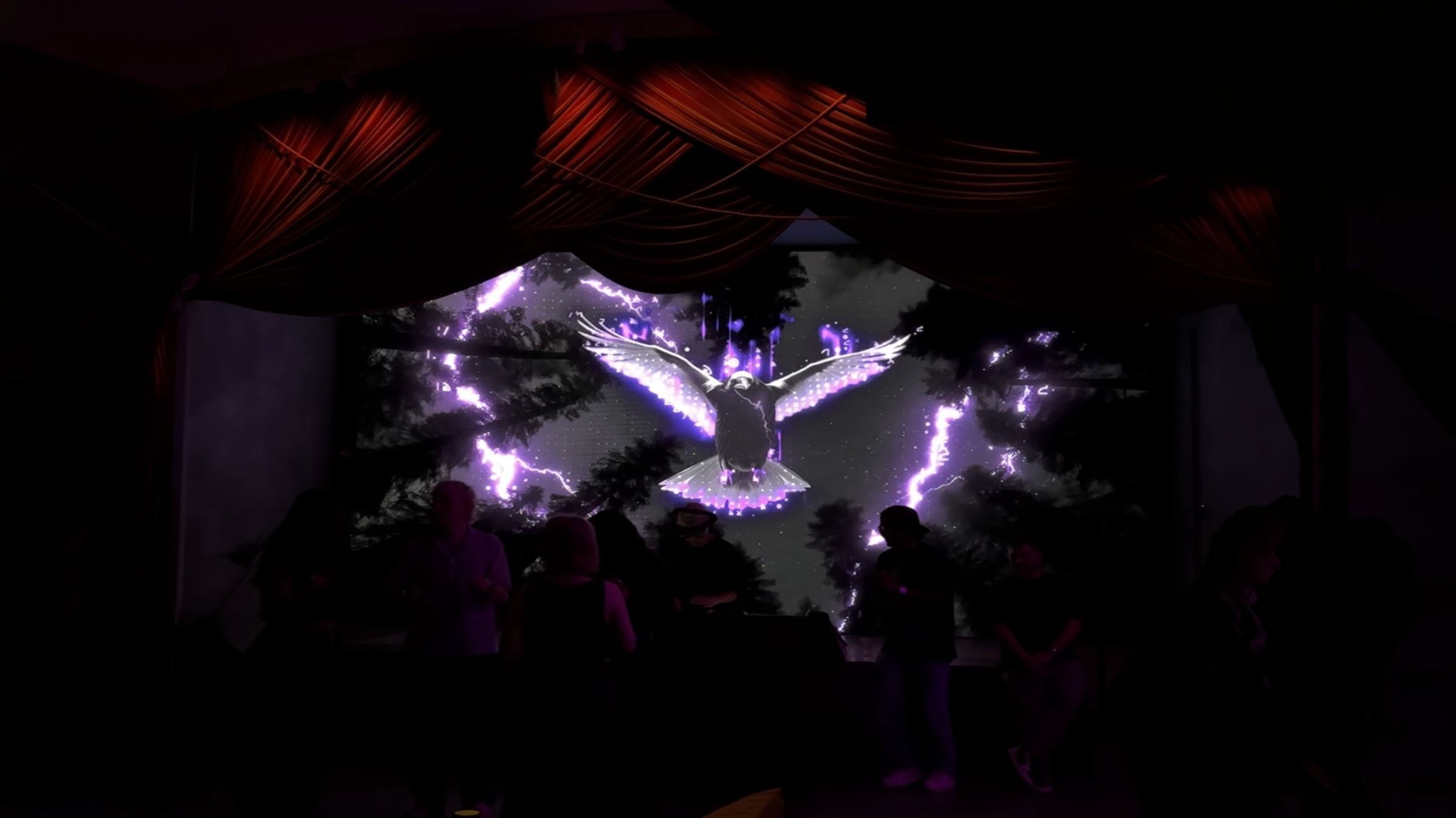 A stage under red drapes with an LED wall showing a bird and purple lightning behind the DJ.