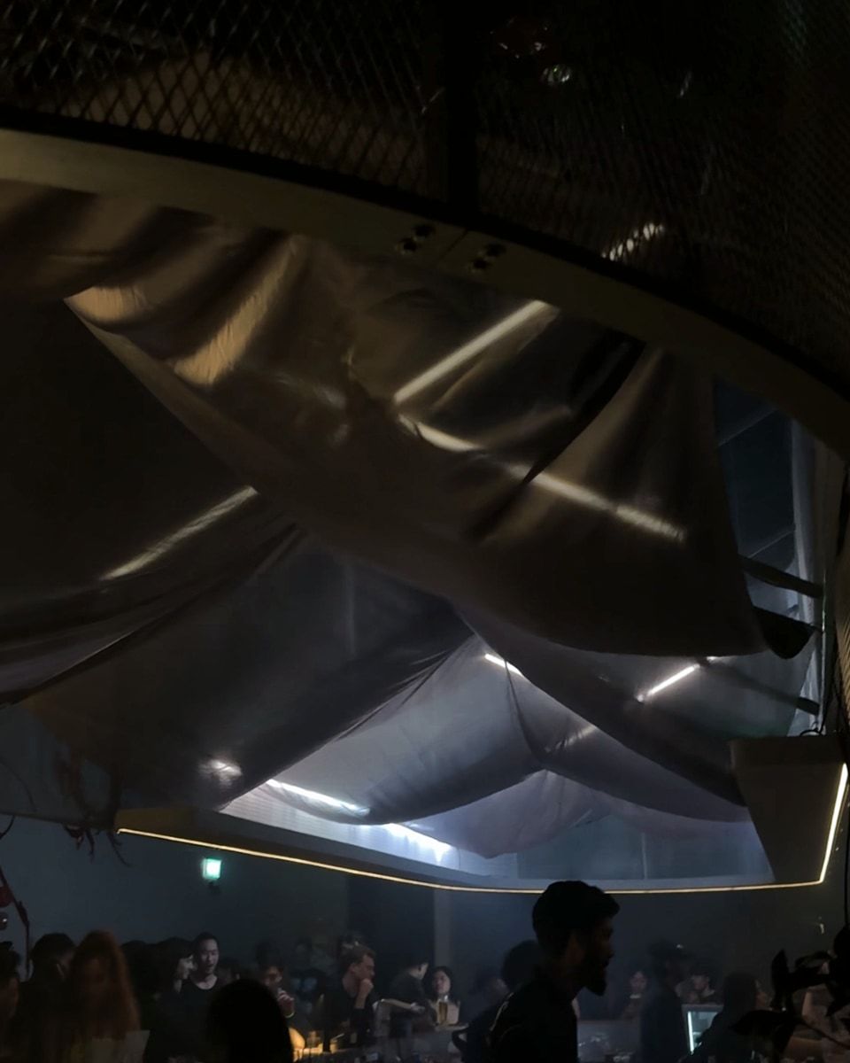 The bar under the mesh drum, with silver fabric and LED tubes overhead and guests below.
