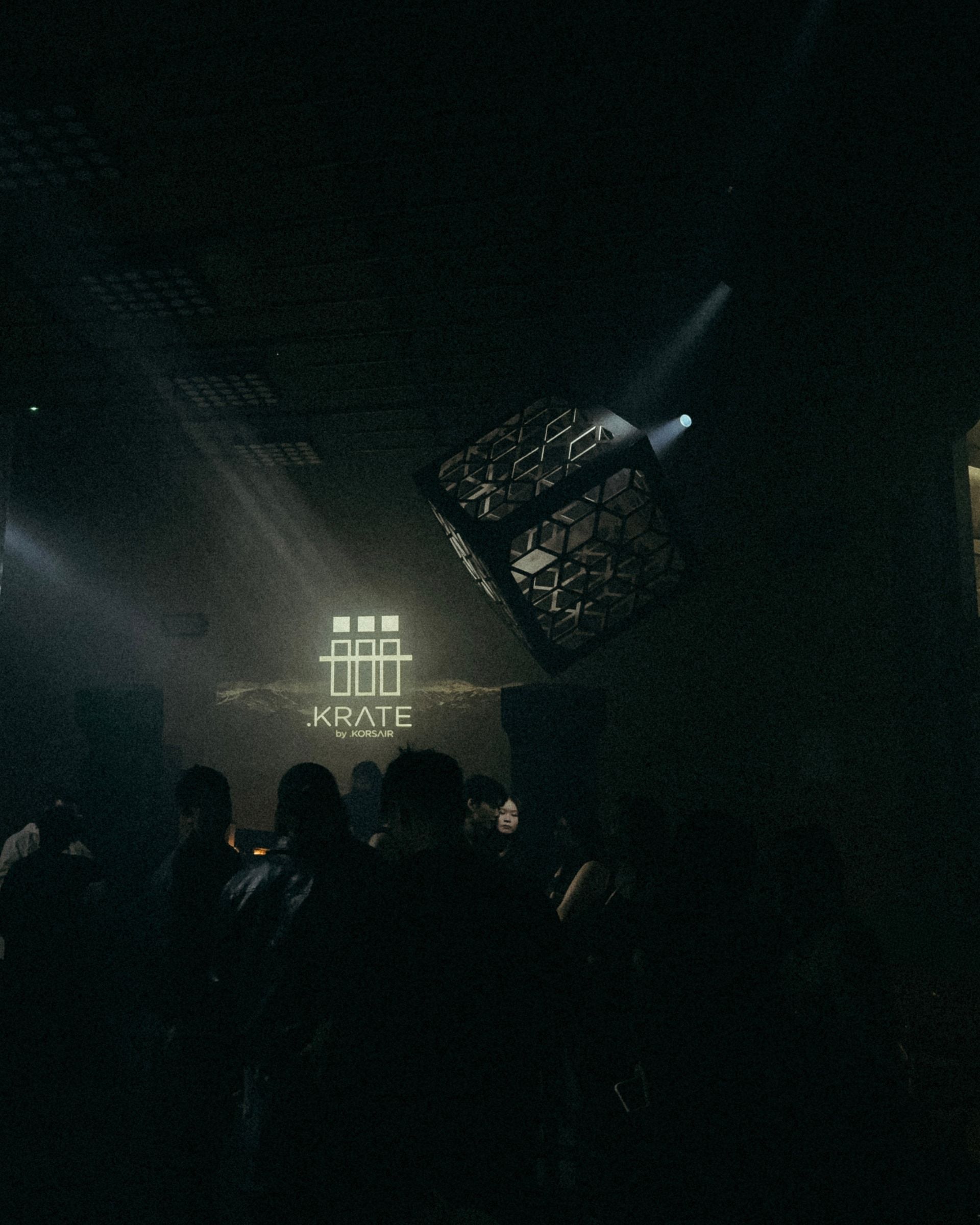 A dark event room with white beams shining through haze above a crowd.