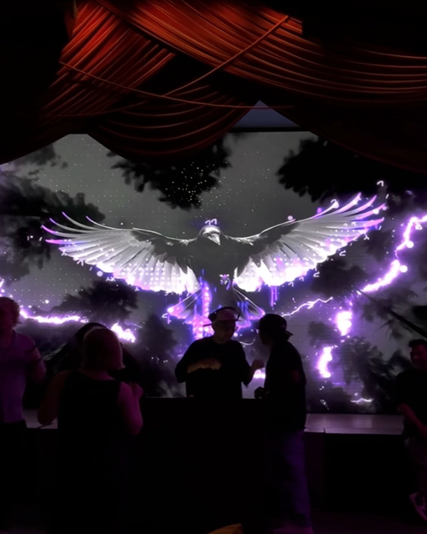An LED wall behind a stage showing a bird with its wings spread and purple lightning.